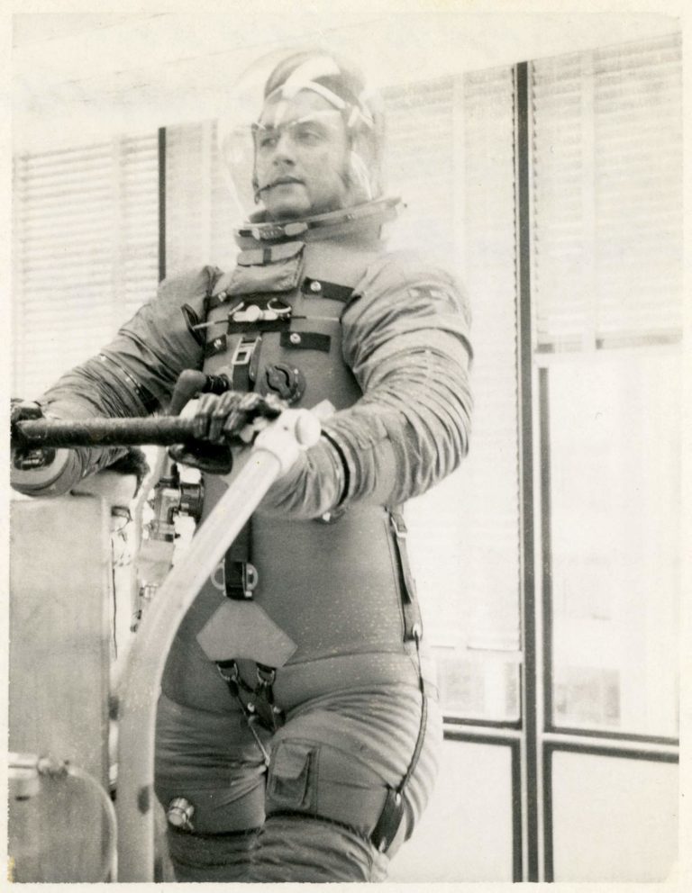 View of Leonard N. Masiello (Hamilton Standard employee) pushing a cart while wearing a a prototype Apollo space suit, Fall 1966. Taken at Hamilton Standard in Windsor Locks, Connecticut.
